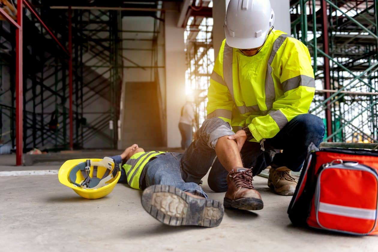Apoyo de primeros auxilios para accidente laboral de trabajador de la construcción en el sitio. El trabajador se cae del andamio al suelo, y el equipo de seguridad ayuda al empleado accidentado.