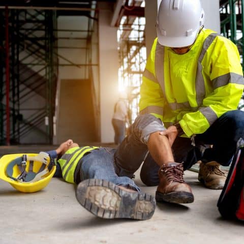 Apoyo de primeros auxilios para accidente laboral de trabajador de la construcción en el sitio. El trabajador se cae del andamio al suelo, y el equipo de seguridad ayuda al empleado accidentado.