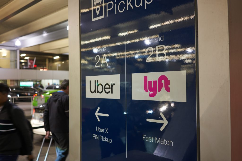 Señal de recogida de pasajeros para servicios de Uber y Lyft en un aeropuerto o zona de transporte. La señal indica las áreas de recogida: 'Isla 2A' para Uber y 'Isla 2B' para Lyft, con flechas señalando las direcciones para cada servicio.