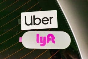Pegatinas de los servicios de transporte Uber y Lyft en la ventana trasera de un coche. El logotipo de Uber aparece en la parte superior, mientras que el de Lyft, en color rosa, está justo debajo.