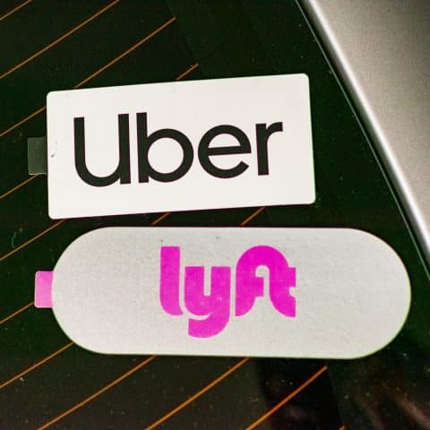 Pegatinas de los servicios de transporte Uber y Lyft en la ventana trasera de un coche. El logotipo de Uber aparece en la parte superior, mientras que el de Lyft, en color rosa, está justo debajo.