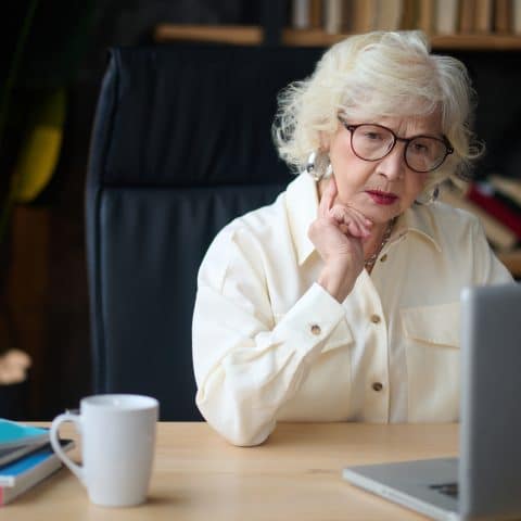 Mujer madura mirando al portátil y tocándose el mentón