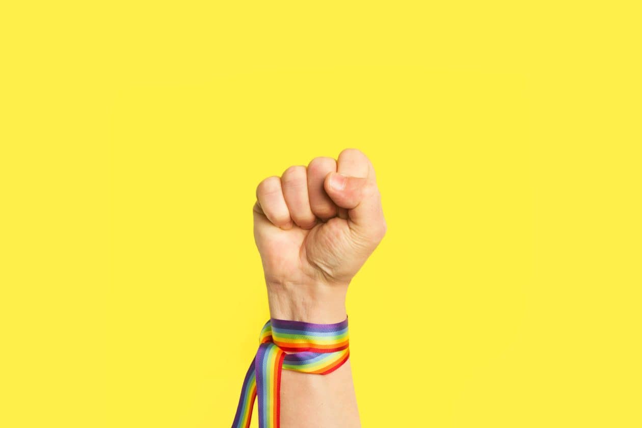 Puño levantado con pulsera de bandera arcoíris LGBT sobre un fondo amarillo brillante liso y aislado. Vista de frente y de cerca