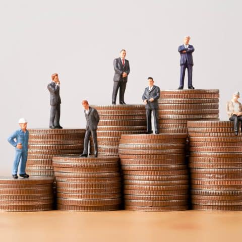 Muchas figuras en miniatura de negocios de pie sobre monedas apiladas para diferentes ingresos y salarios en cada posición.