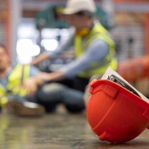 Enfocar el casco de seguridad rojo con los trabajadores de fábrica heridos desenfocados de fondo.