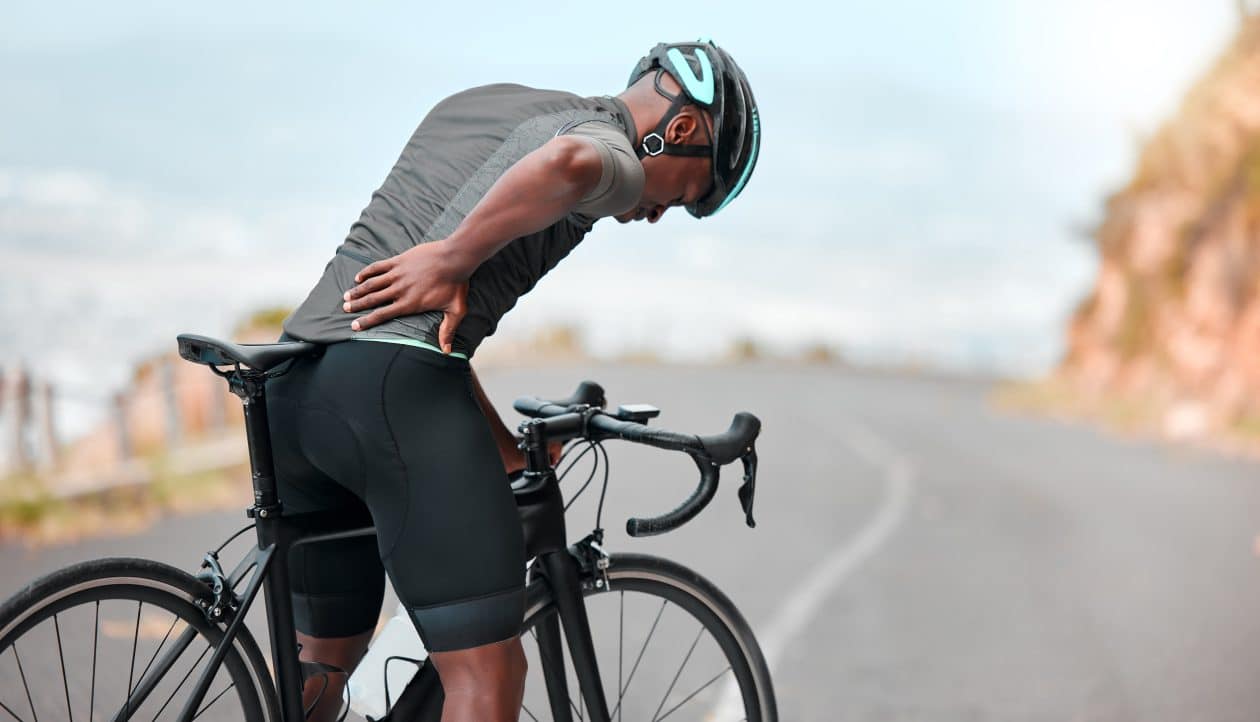 Aptitud, lesiones deportivas y dolor de espalda: el ciclista experimenta incomodidad mientras pedalea por una ruta montañosa. Entrenamiento, dolor y un atleta lesionado sufriendo de molestias en las articulaciones, los músculos y la columna vertebral.
