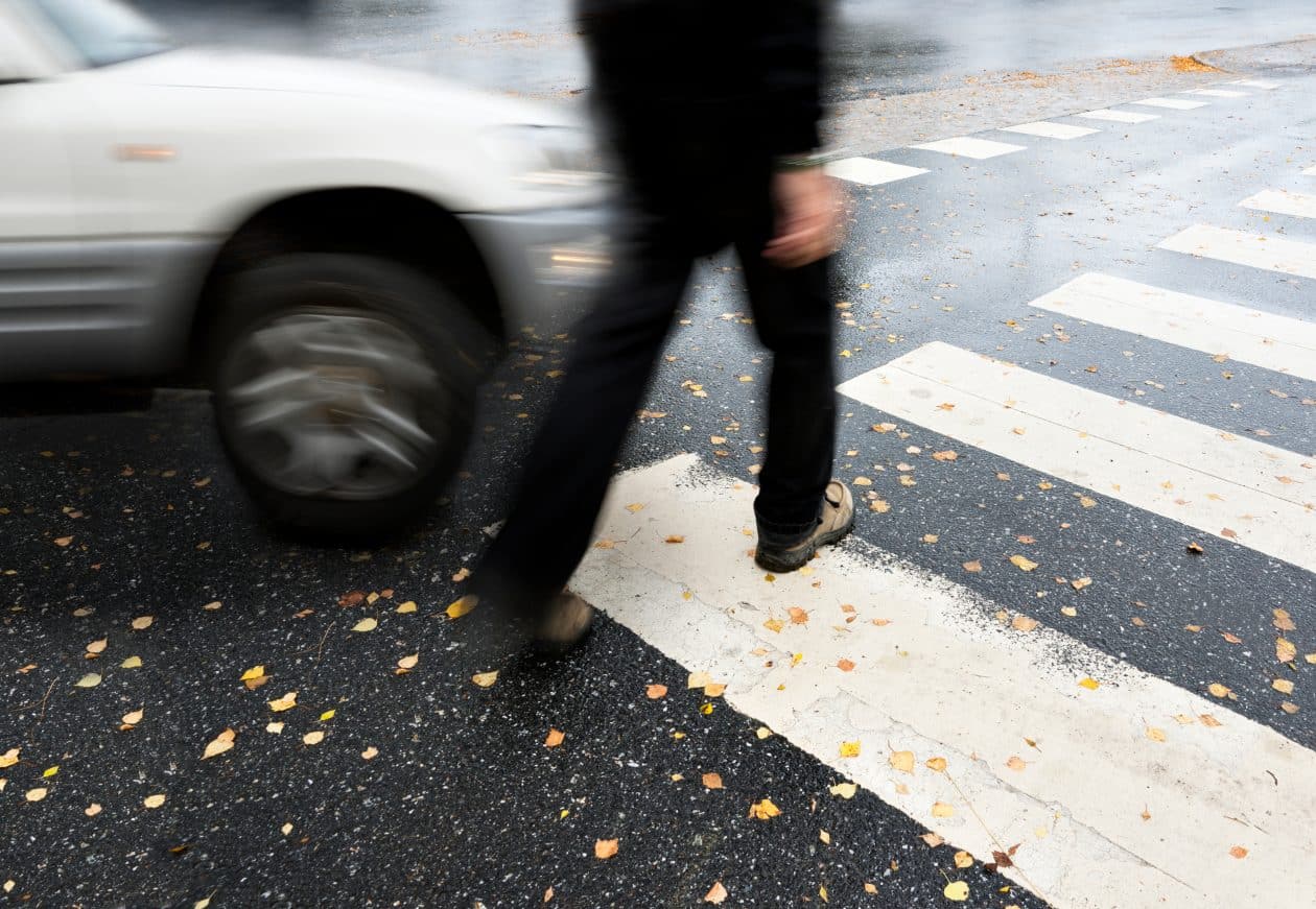 Persona cruzando un paso de peatones mientras un coche se acerca a gran velocidad. La imagen captura el movimiento borroso del vehículo y del peatón, lo que sugiere una situación de peligro o posible accidente en una intersección.