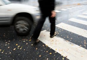 Persona cruzando un paso de peatones mientras un coche se acerca a gran velocidad. La imagen captura el movimiento borroso del vehículo y del peatón, lo que sugiere una situación de peligro o posible accidente en una intersección.