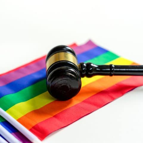 Mazo de madera de abogado sobre banderas de orgullo arcoíris coloridas en fondo blanco, concepto de reclamaciones del movimiento comunitario LGBT por la igualdad, derechos en la corte o legal para la vida, el amor, la familia y el matrimonio de personas LGBTQ.