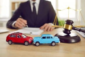 Primer plano de dos coches de juguete sobre el fondo de un juez que está dirigiendo un juicio por un accidente de tráfico.