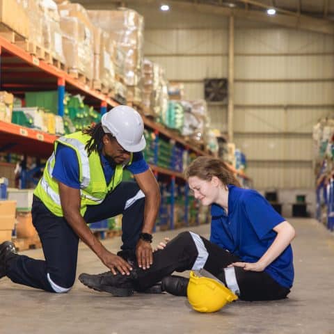 Joven mujer trabajadora de almacén accidente lesión en la pierna resbalón y caída esguince en el tobillo amigo ayuda apoyo